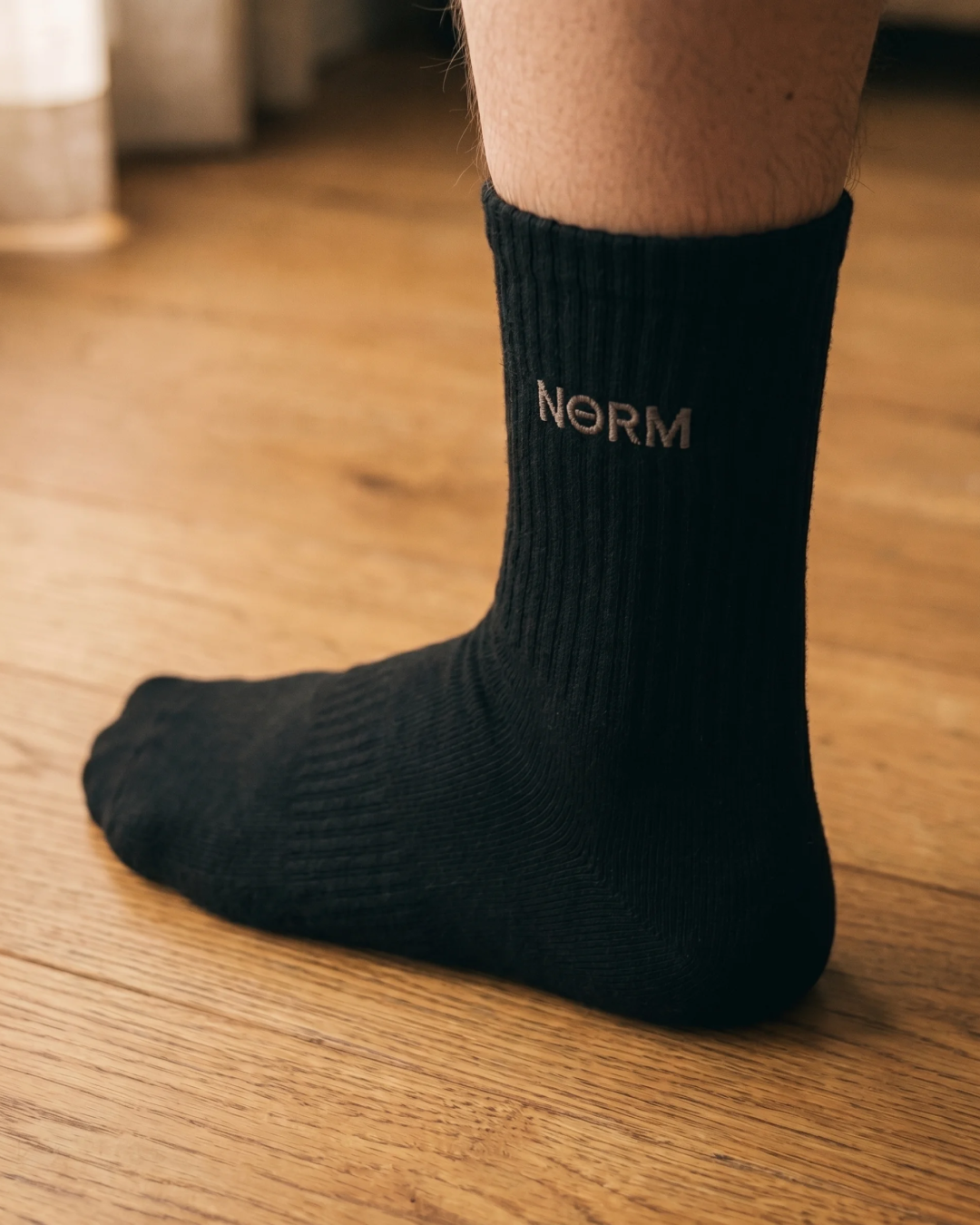 NƟRM Everyday Crew black at three-quarter angle, reinforced heel and toe visible.
